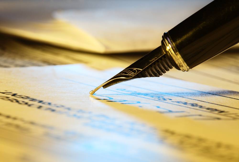 Close-up of a fountain pen signing a document or check on a desk.