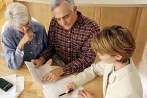 Three people sit at a table reviewing documents together in a well-lit room.
