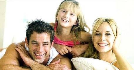 A man, a woman, and a young girl are smiling and posing closely together indoors.